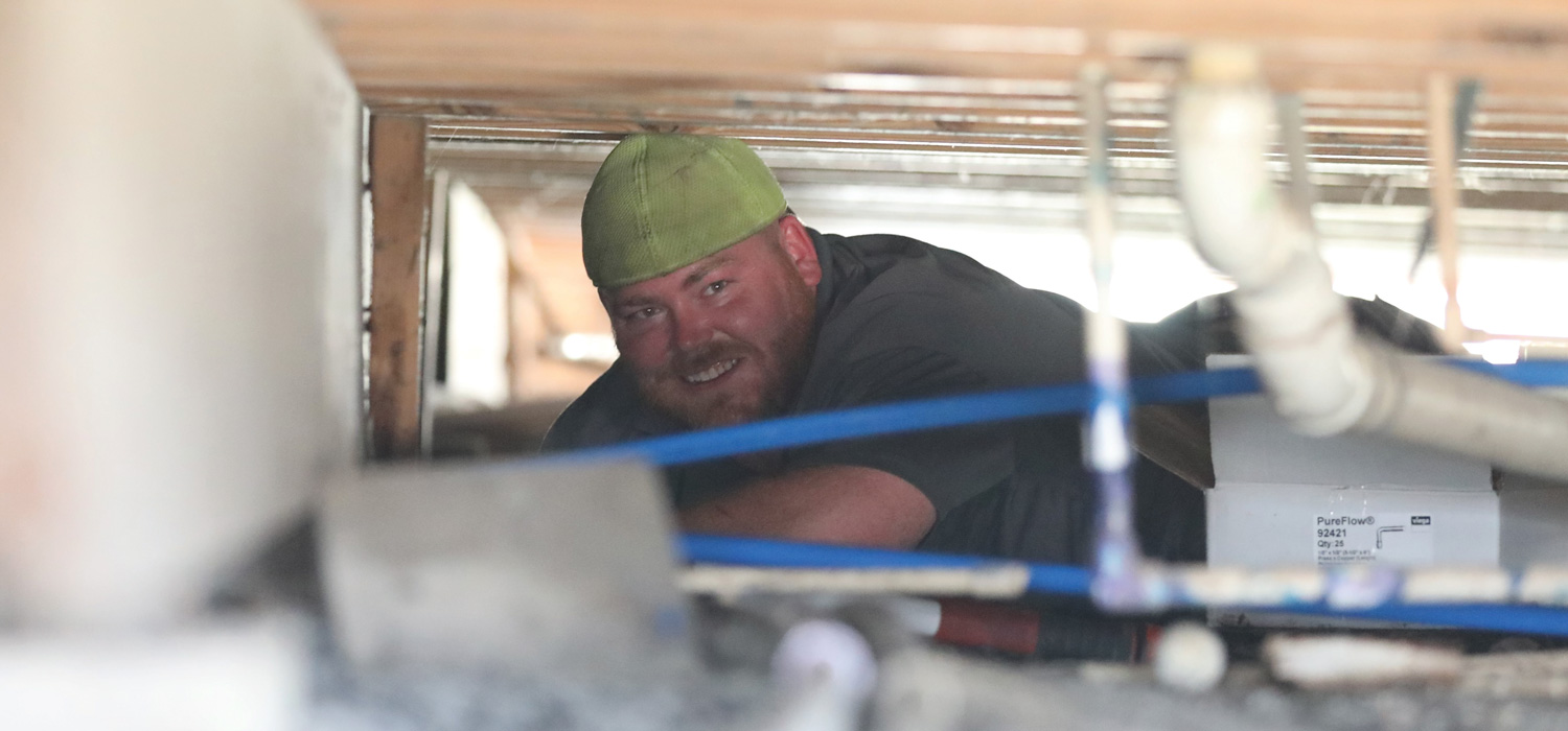 A Forth Worth volunteer in a green cap replacing damaged pipes underneath a home in Austin, Texas to aid disaster victims