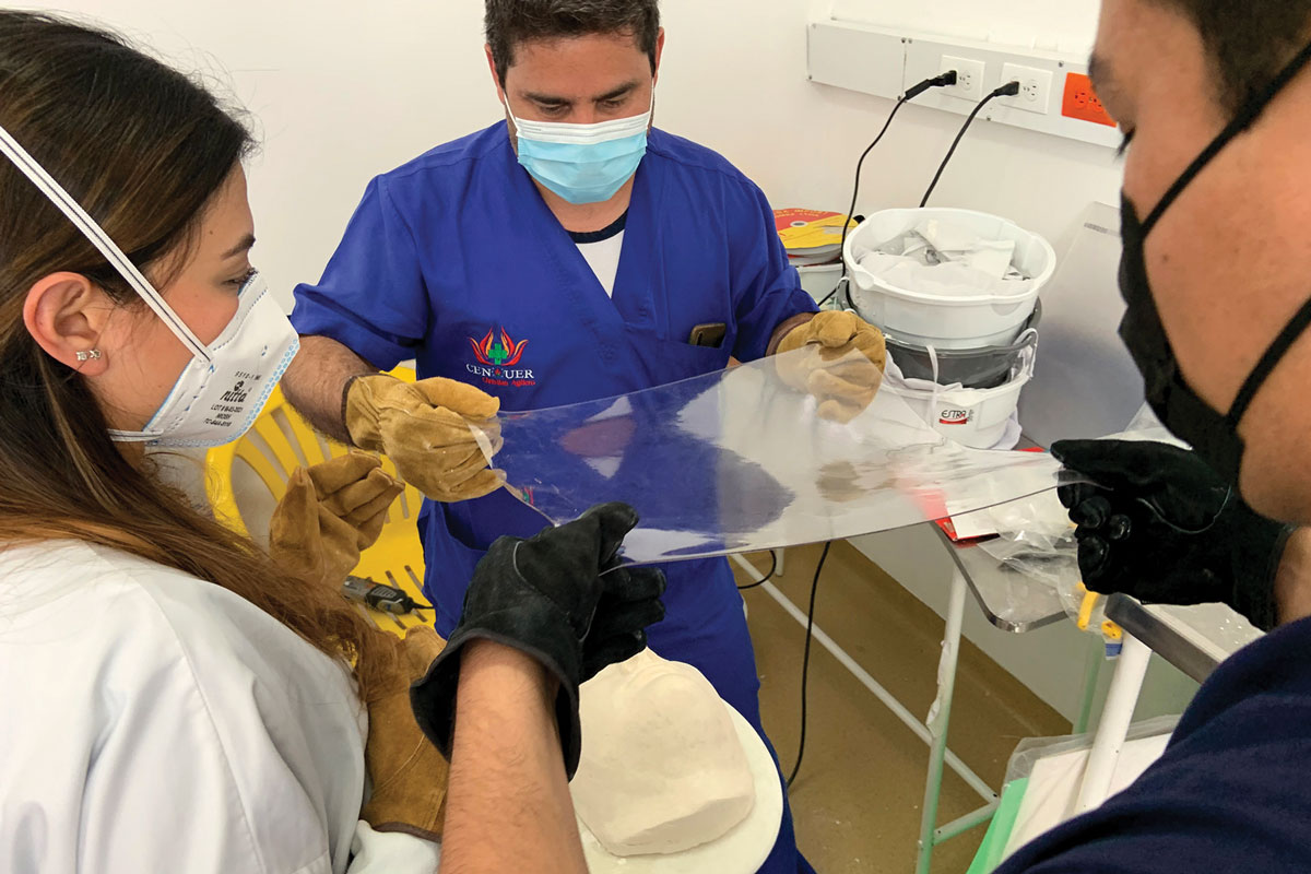 Participants at the Physicians for Peace workshop have warmed up the PETG sheet to be draped and pressed over the plaster mold to create the facemask