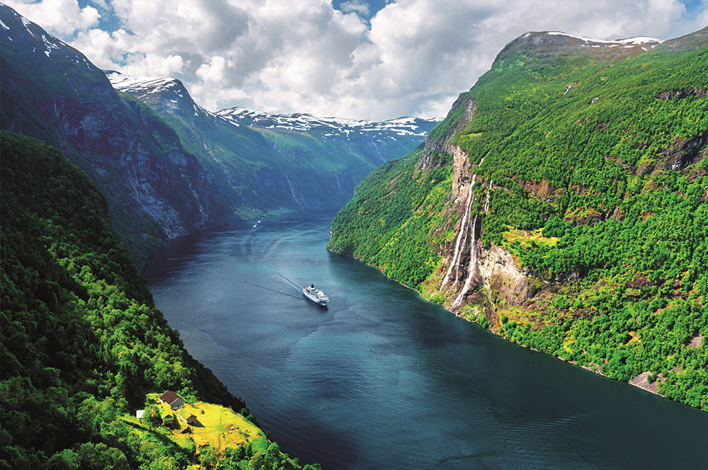 Cruise ship in water between lush green mountains
