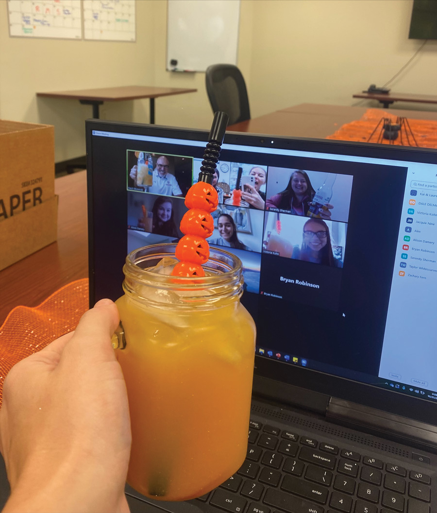 hand holding a cocktail with a jack-o-lantern straw during a virtual happy hour