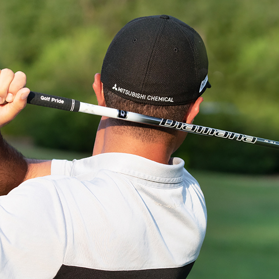 back view of a man at the end of a golf swing, he wears a cap with the Mitsubishi Chemical Group logo embroidered on the back