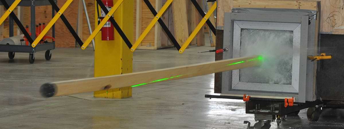 a piece of lumber being shot into a window in a warehouse lab for testing