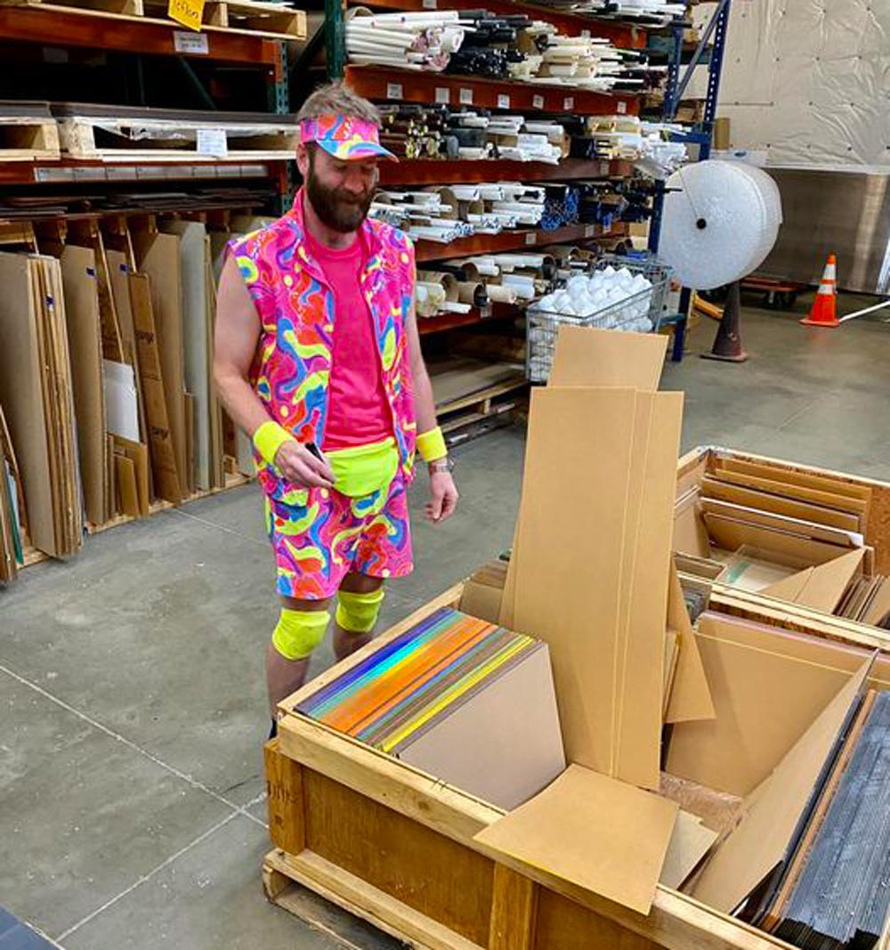 man dressed in neon colored clothes standing near a wooden box of plastic scrap 