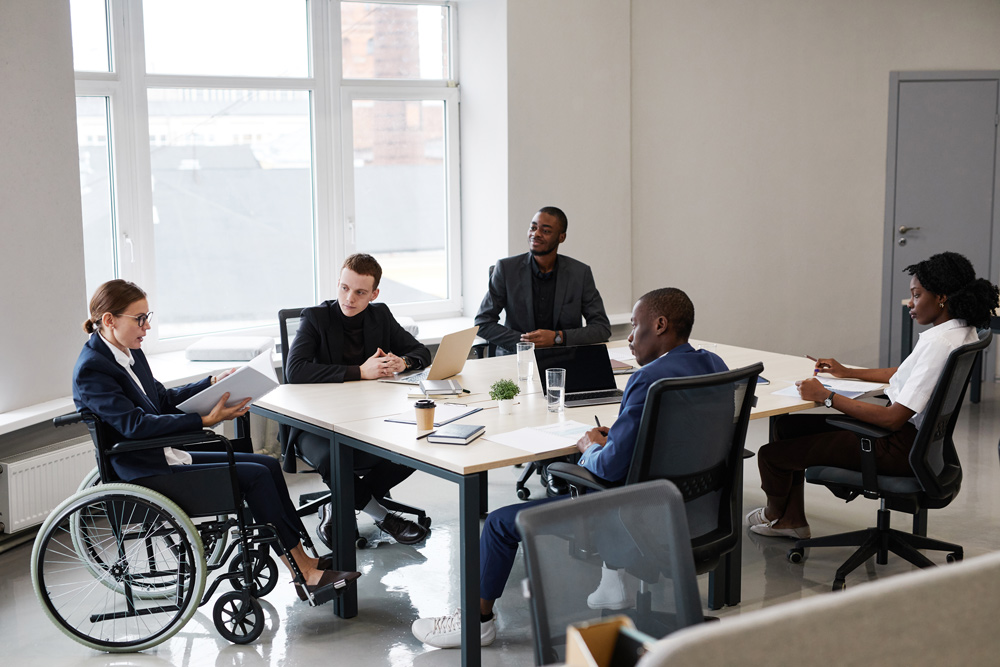 group of people in a meeting listening to a woman in a wheelchair speak 