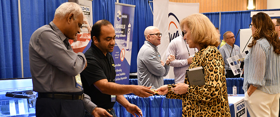 A convention attendee receives a handout from an exhibitor at a trade show booth.