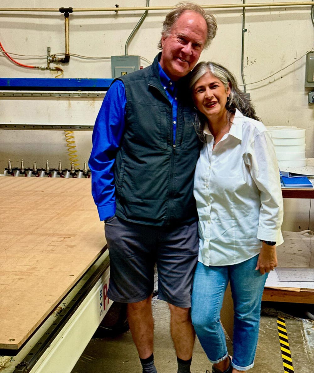 Drew and Anita Schwartz lean together for a photo standing beside a large machine in a factory