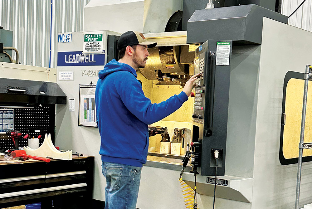a man stands at a large CNC mill with raw UHMW blocks for fabrication, pressing buttons on a console