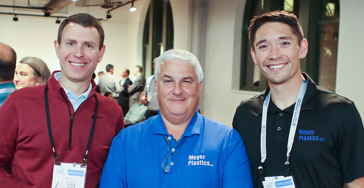 Three smiling men pose together at the IAPD convention. The man in the center wears a blue polo and the man on the right wears a black polo, both featuring "Meyer Plastics Inc." logos. All three wear conference name badges.