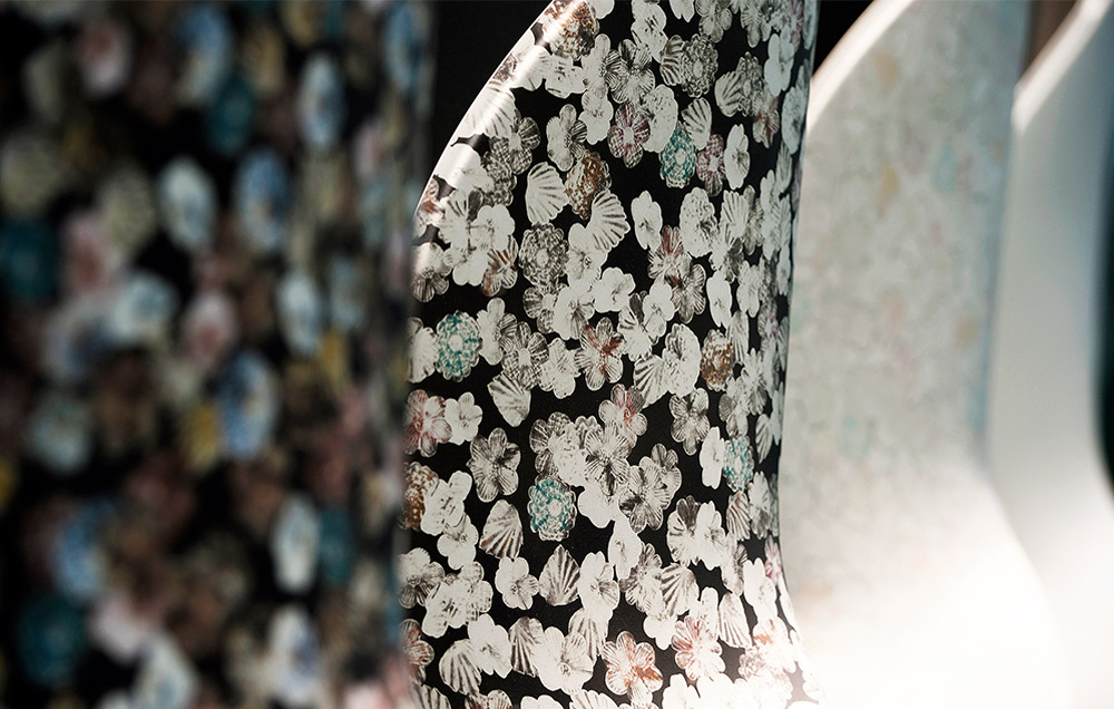 A close-up side view of curved KYDEX thermoplastic surfaces featuring Infused Imaging, displaying a dense, decorative pattern of small white, brown, and blue flowers against a black background.