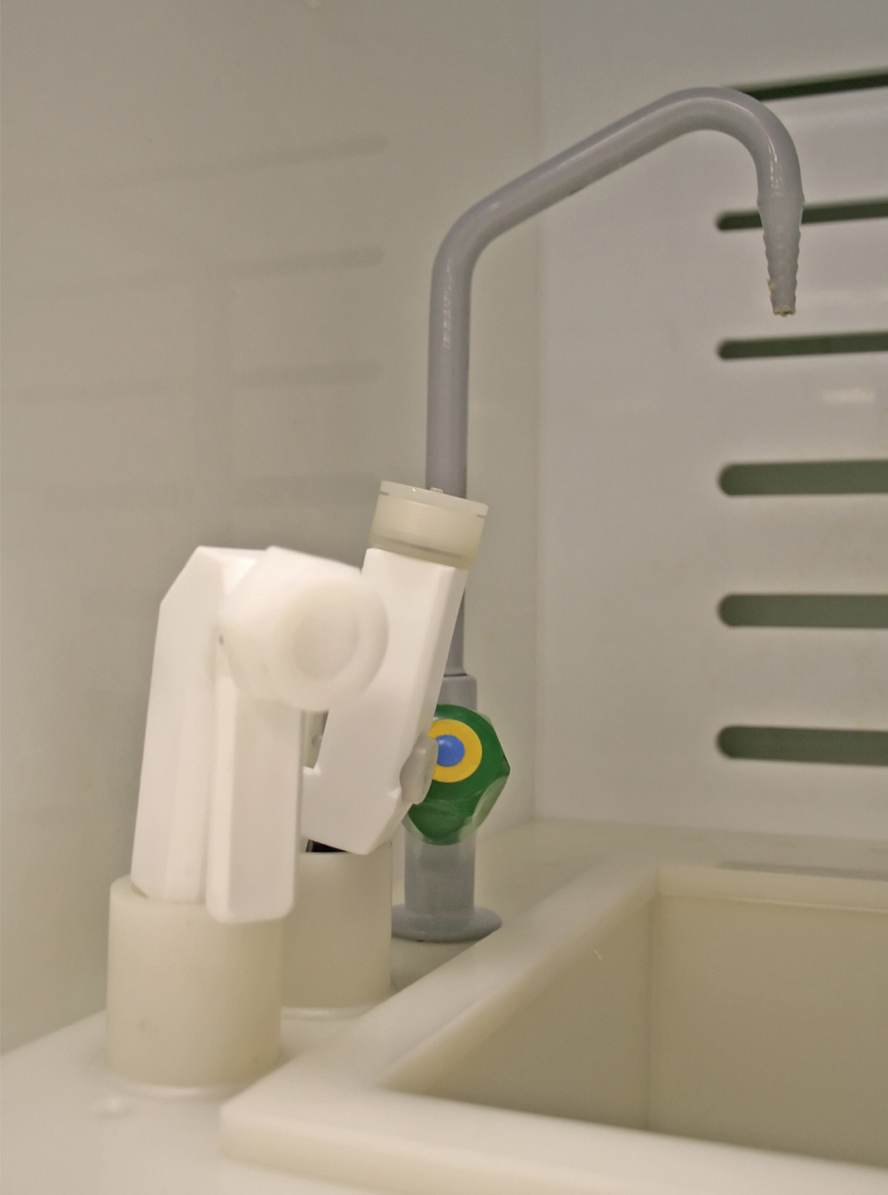 A laboratory wet bench featuring a white PVDF sink and a specialized white PTFE nozzle. A grey curved spout is mounted behind the basin against a slotted white wall, illustrating chemical-resistant components in a cleanroom environment.