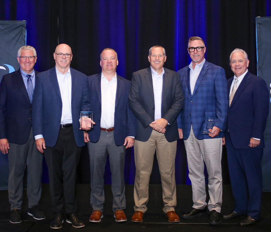 Four Plaskolite representatives stand between two presenters against a blue backdrop.
