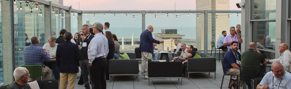 Attendees at the IAPD Convention network on a rooftop terrace at sunset, with views of the city skyline.