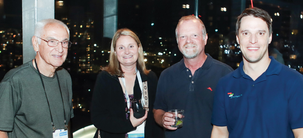 Four conference attendees smile for a group photo against a backdrop of city lights at night.