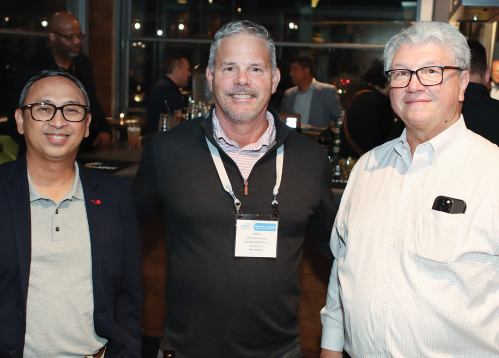 Three men in business casual attire smile for a portrait at a nighttime networking event.