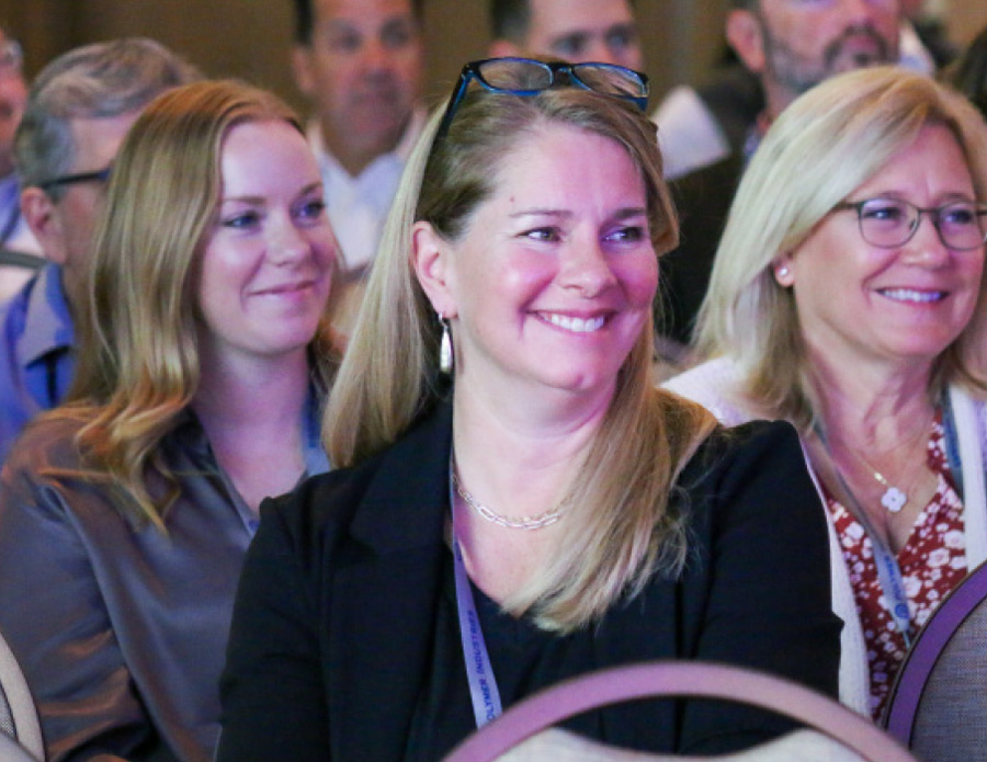 zoomed in view of three women smiling as audience members in a conference like setting