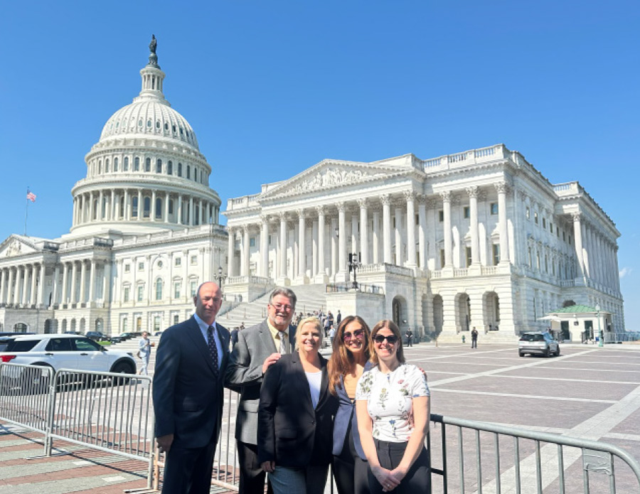 five people take a group photo in a large blockaded plaza in front of a large white domed and pillared building