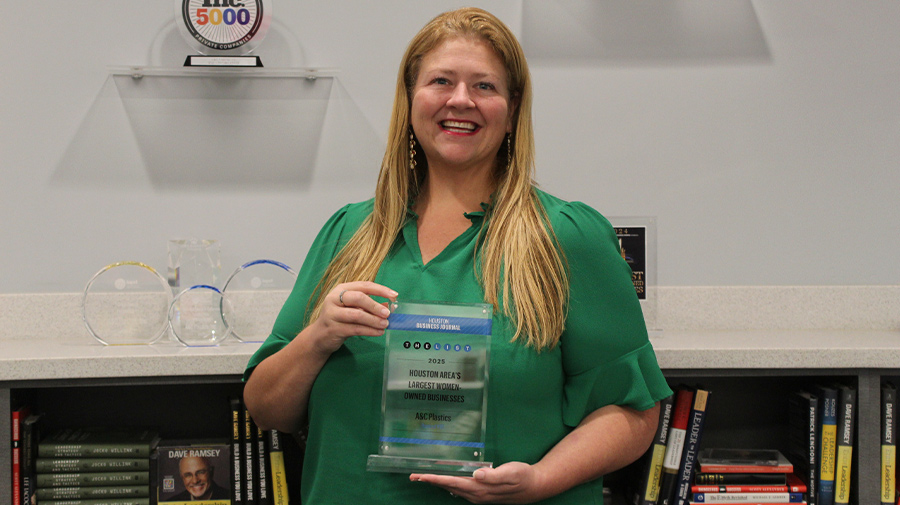 Katie Clapp smiles while wearing a green blouse and holding a glass award