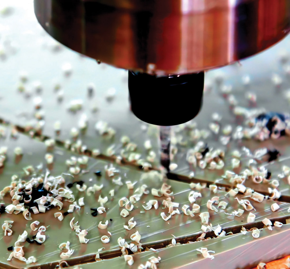 A close-up of a high-speed milling machine cutting a metallic surface, producing a large amount of curly metal swarf and chips across the work area during the machining process.