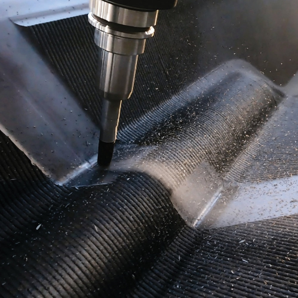 Close-up of a CNC milling tool precisely smoothing and shaping the ribbed surface of a 3D-printed composite part, with fine material shavings visible during the process.