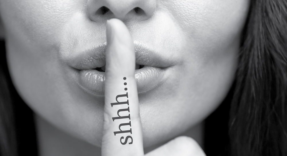 Close-up of a face with a finger over lips, signaling silence.