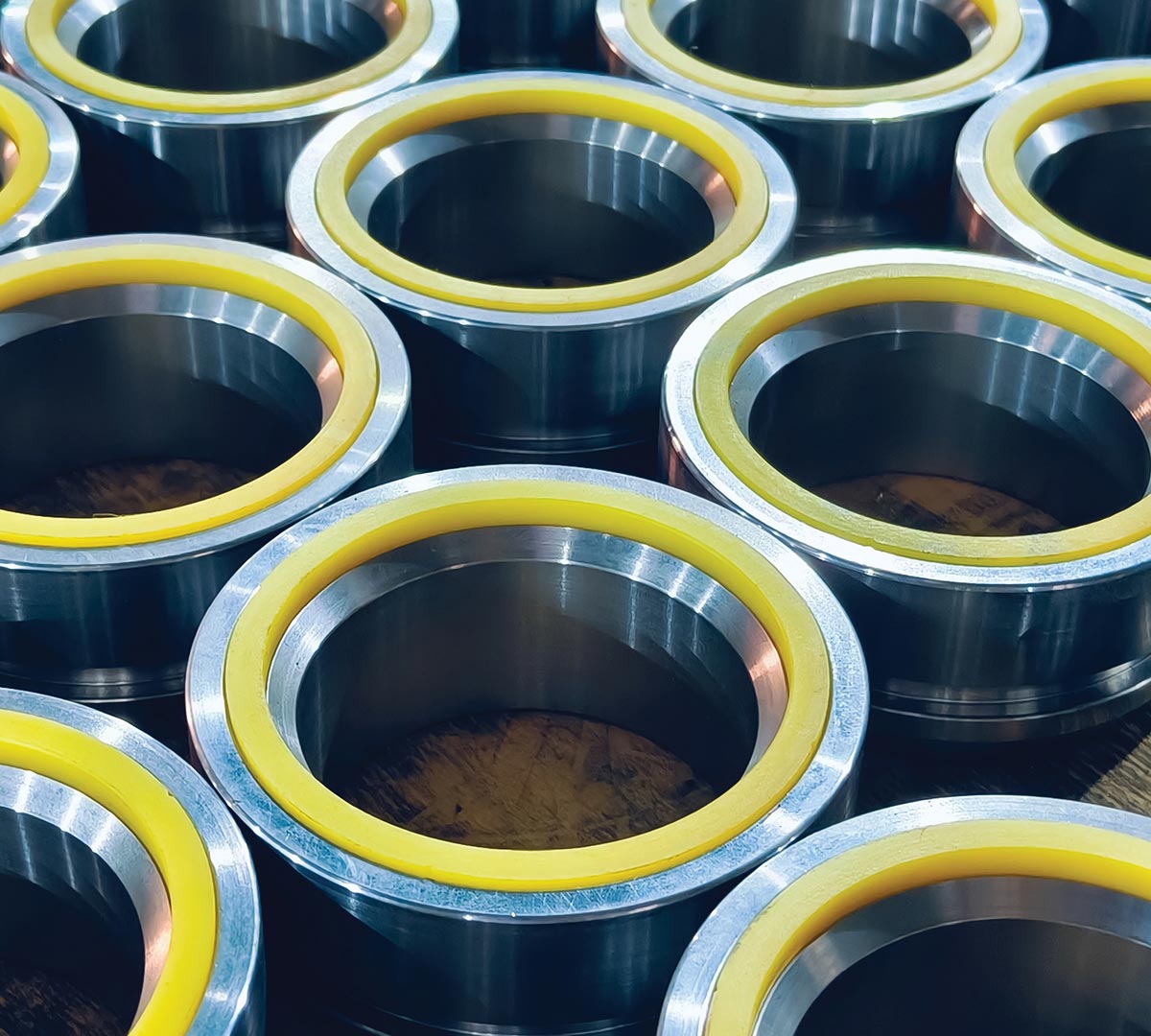 Rows of cylindrical metal industrial components featuring polished silver exteriors and vibrant yellow inner linings.