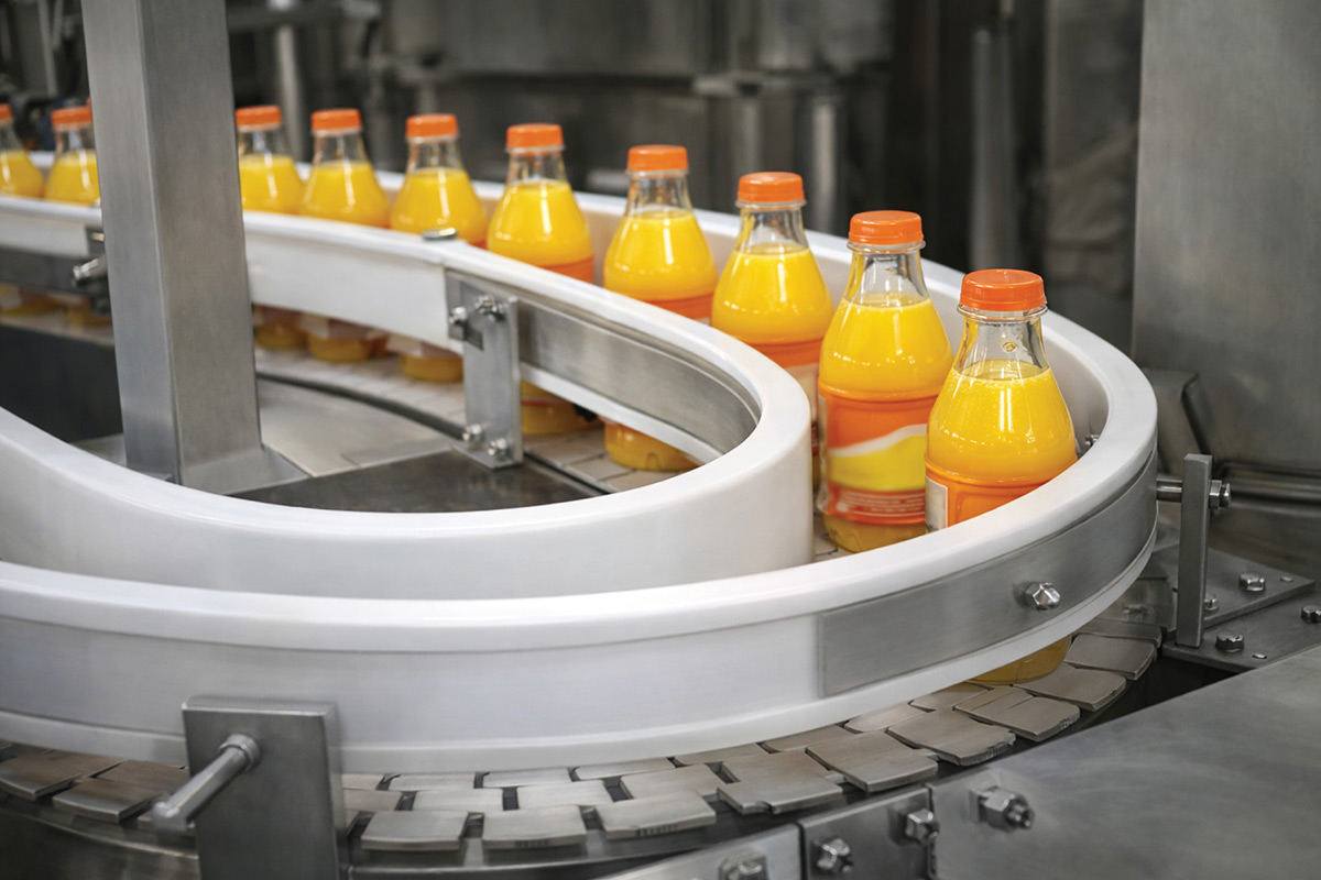 Bottles of orange juice with orange caps moving along a curved white conveyor belt in an industrial food production facility