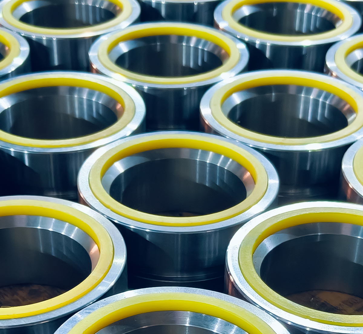 Rows of identical cylindrical metal components, each fitted with a yellow plastic ring around the top rim.