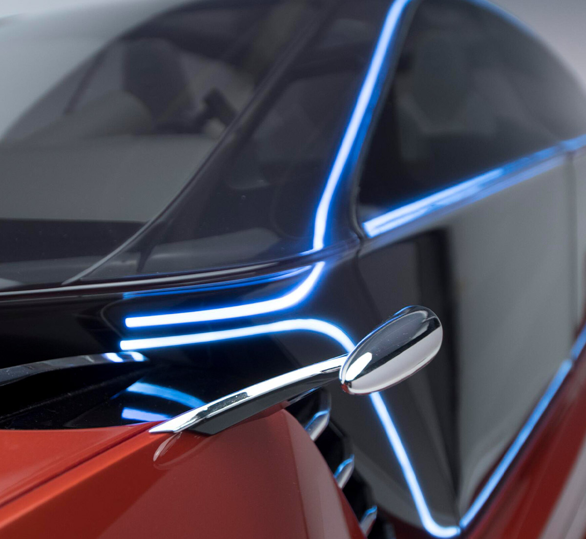 Close-up profile of a futuristic concept car featuring red body panels, a dark wrap-around windshield, and illuminated blue accent lines integrated into the vehicle's exterior trim.