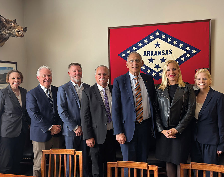 Seven professionals posing in an office in front of an Arkansas flag.