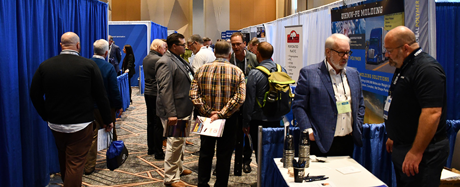 Attendees browsing vendor exhibition booths in a crowded convention hall.