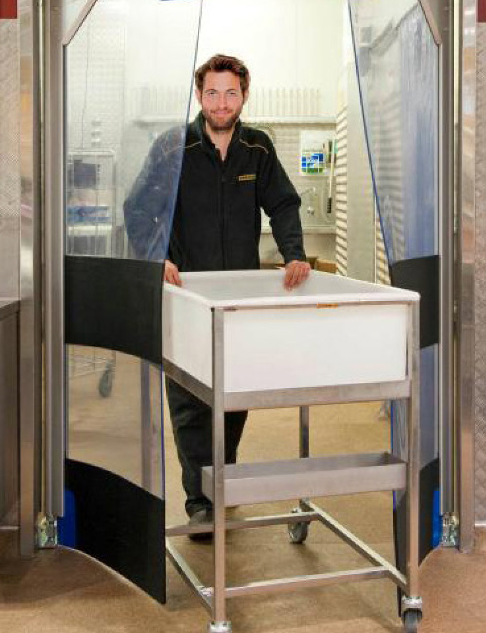 Man pushing a white utility cart on wheels through a set of flexible clear plastic swinging doors.