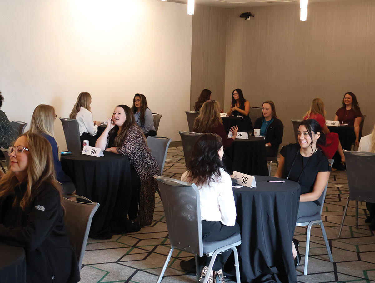 Women seated in pairs at small numbered tables participating in a speed-networking session inside a conference room.