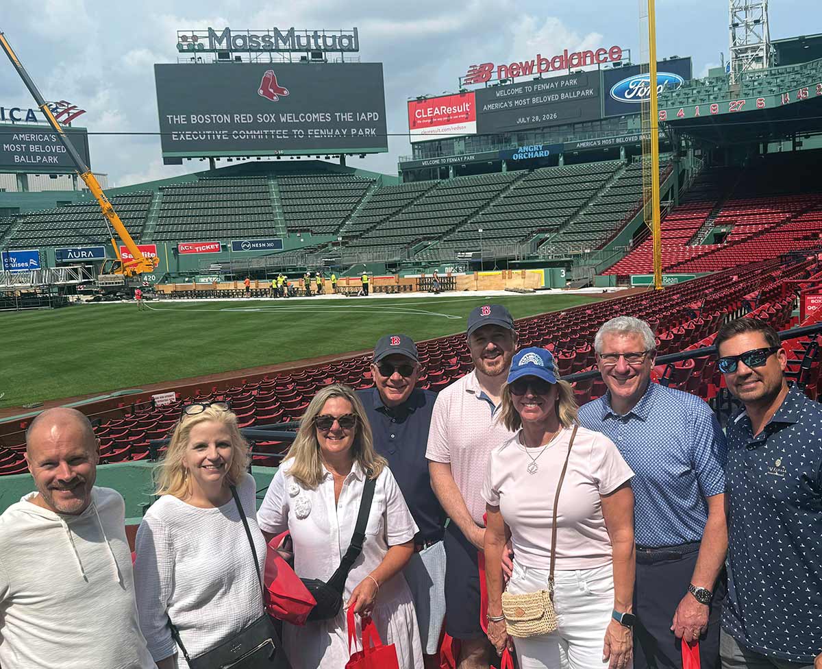 A group posing in the stands at Fenway Park with a welcome message on the stadium scoreboard.