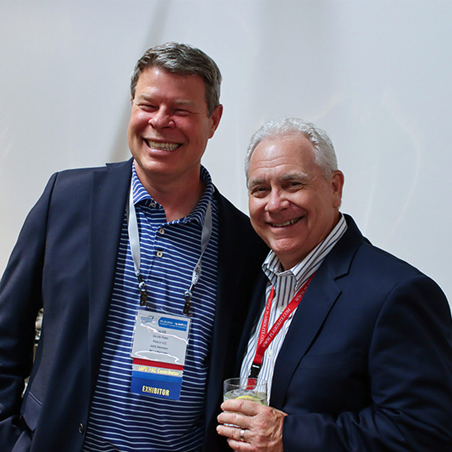 Two men wearing conference badges smiling together at a social event.